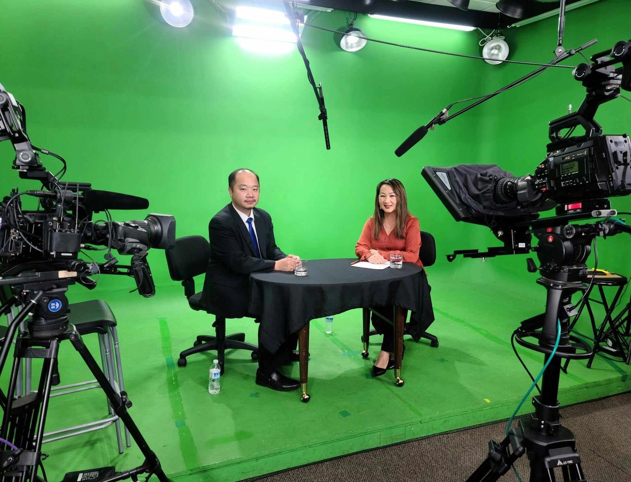 Asian man and woman in a green room with cameras for news filming