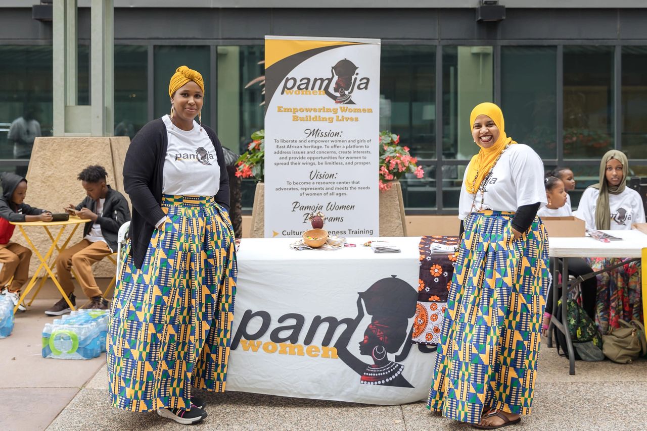 Two women in front of a Pamoja Women table smiling