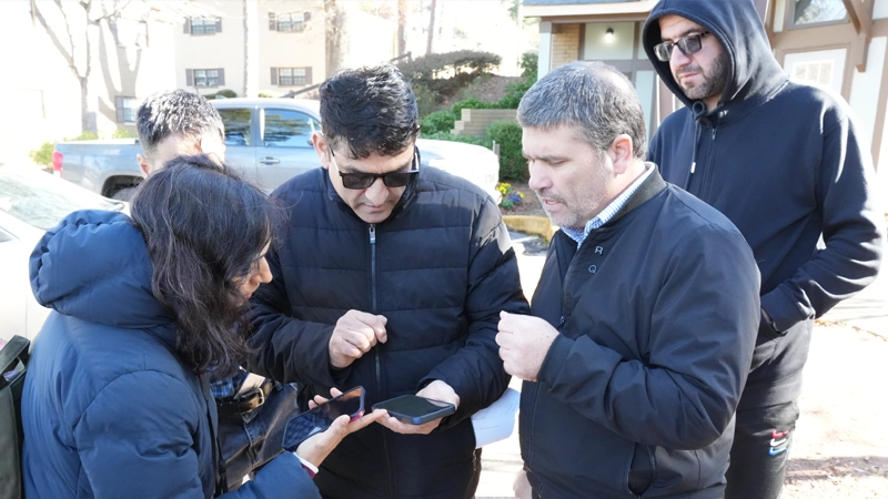 Woman and 4 men gathered outside an apartment building looking at their cell phones together and talking.