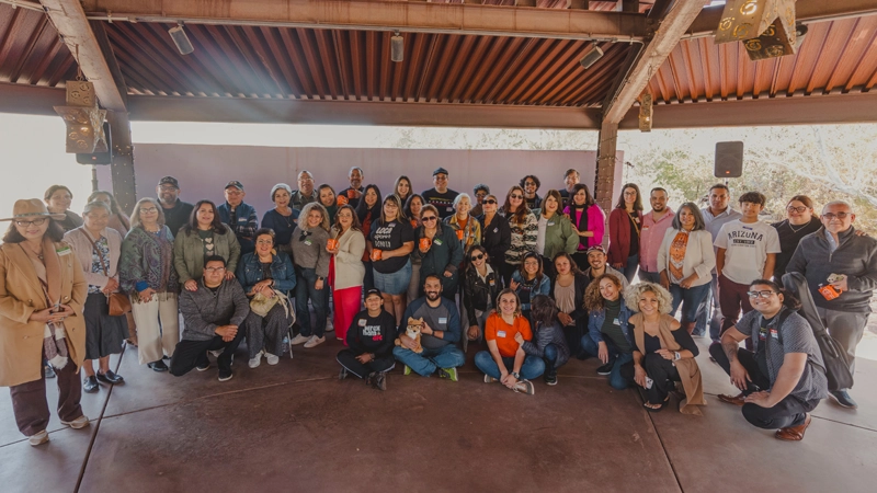 Diverse group of people gathered and smiling under an outdoor pergola.