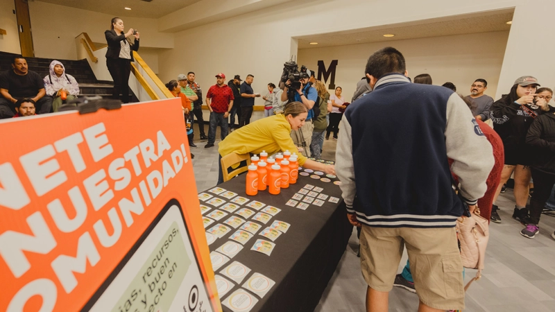 Woman bending over a table with informational materials as she speaks with an interested person at a community event.