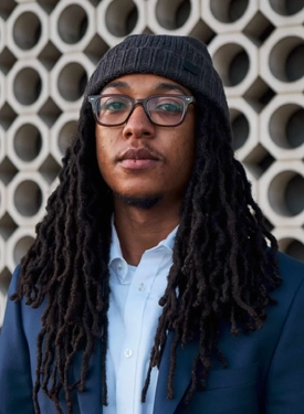 Young Black man with long braids wearing a knit cap, buttondown shirt, blazer and glasses