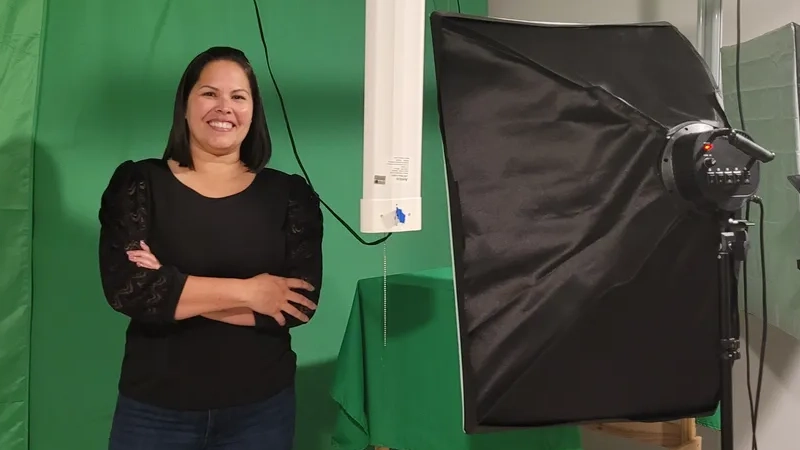 Latina woman smiling in front of a green screen in a studio.