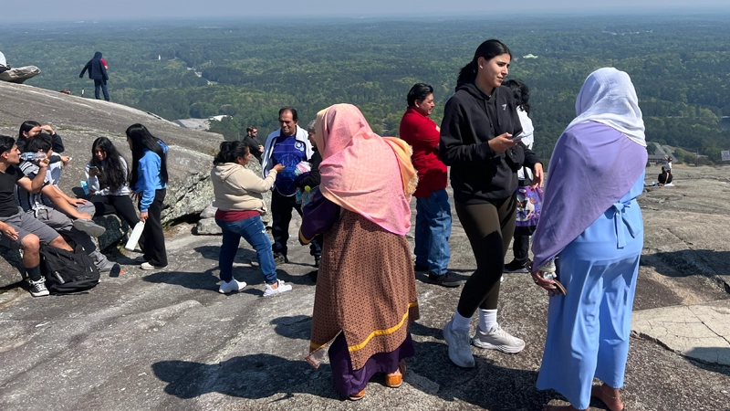 Small crowd of people gathered at the top of a mountain overlooking a valley below.
