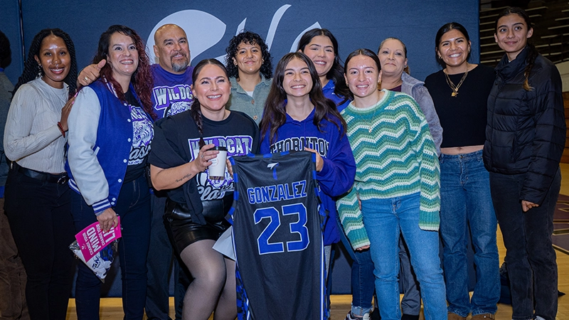 High school students and adults pose for a photo smiling and holding sports jerseys.