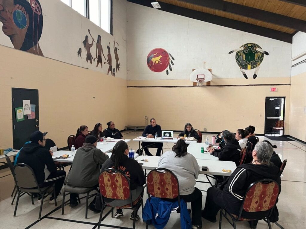 Indigenous community members and Pivot Fund researchers seated around a table in a Native community room discussing their views.