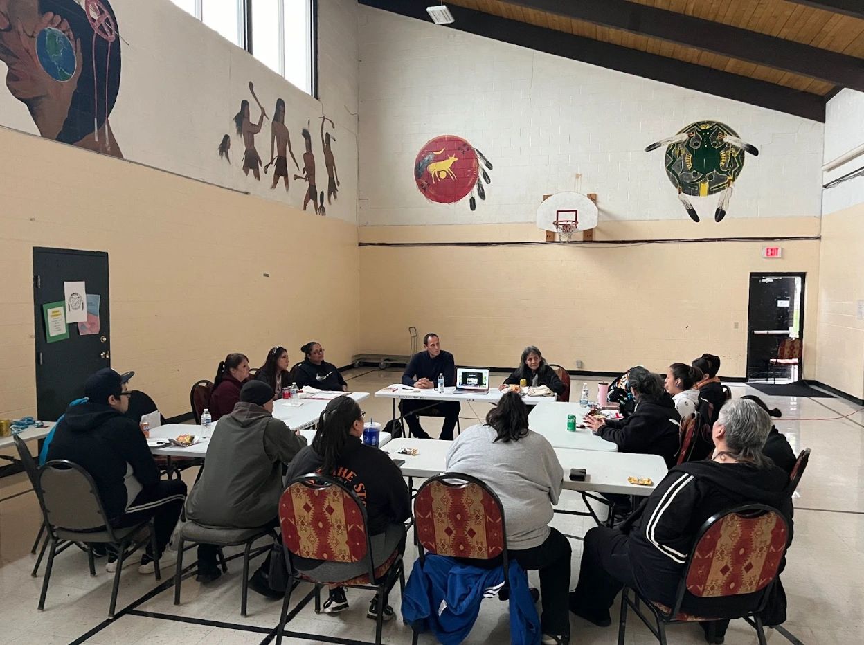 Indigenous community members and Pivot Fund researchers seated around a table in a Native community room discussing their views.