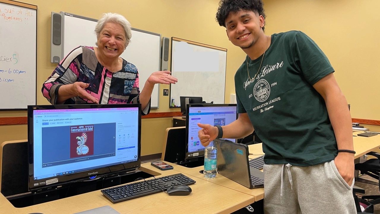 Teenage boy and mature woman smile with thumbs up next to a computer monitor showing artwork.