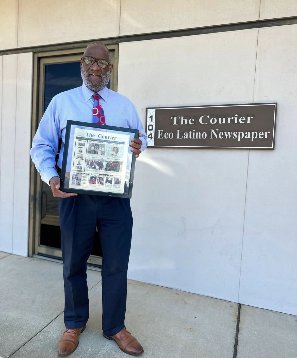 Black man stands in front of The Courier Eco Latino Newspaper sign