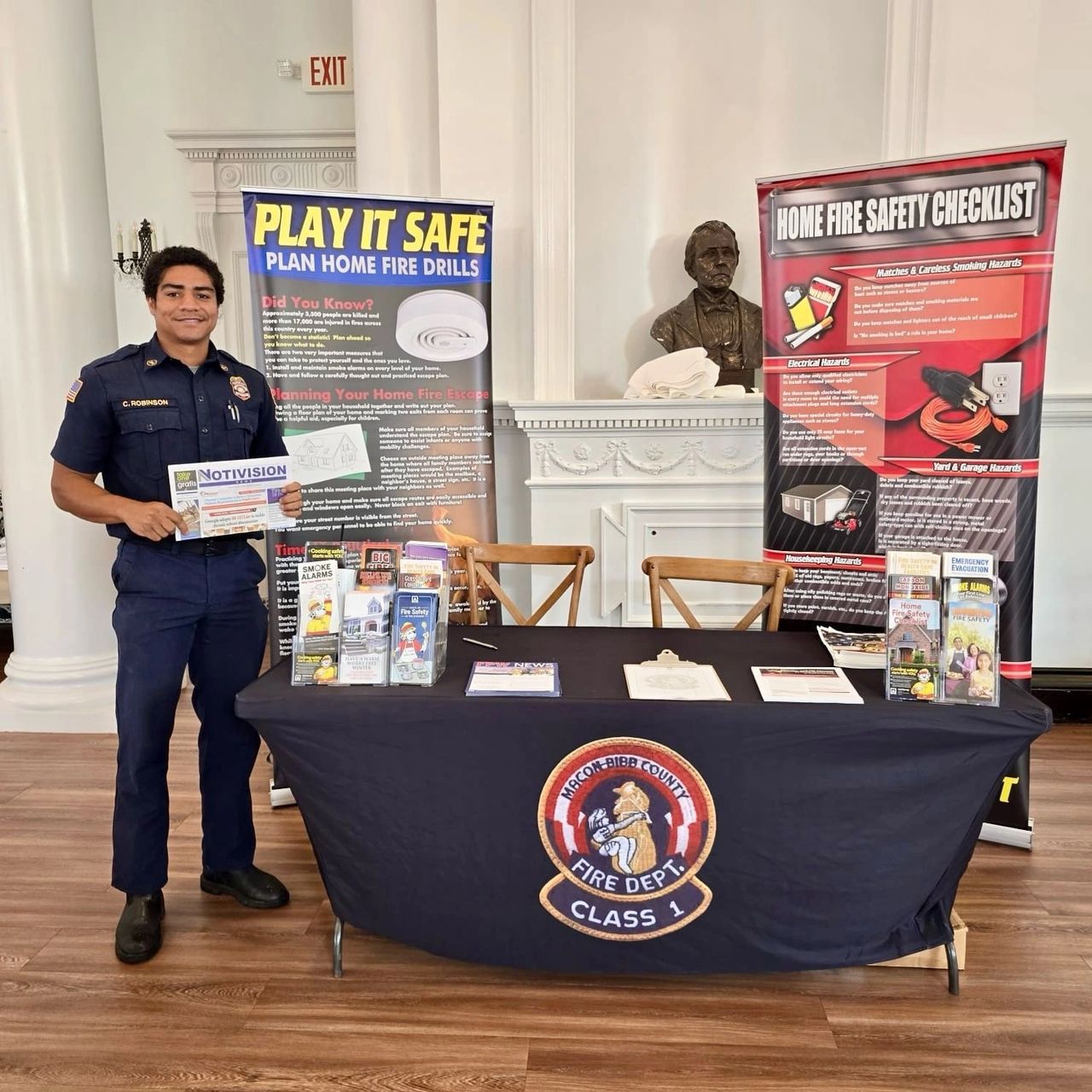 Young male police officer stands in front of a table with banners and information about public safety