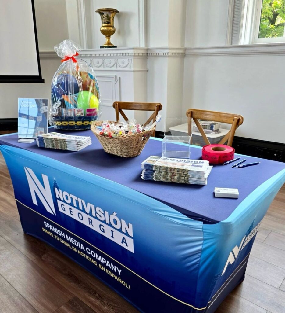 Table with informational materials and swag with NotiVisión Georgia name on the tablecloth