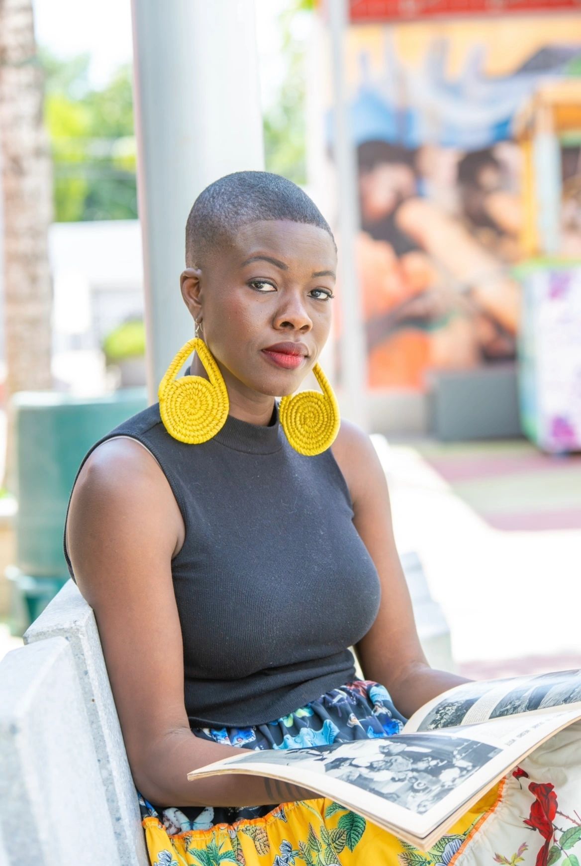 Black woman with shaved head and large expressive yellow earrings looking up from reading a magazine