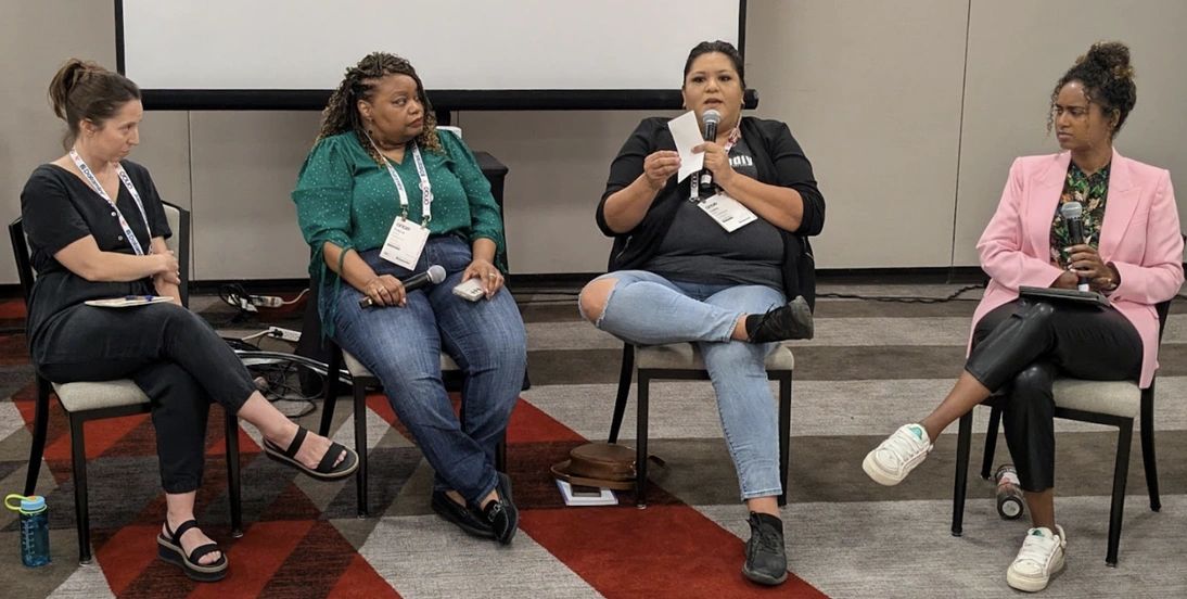 Four women seated in an informal presentation with microphones