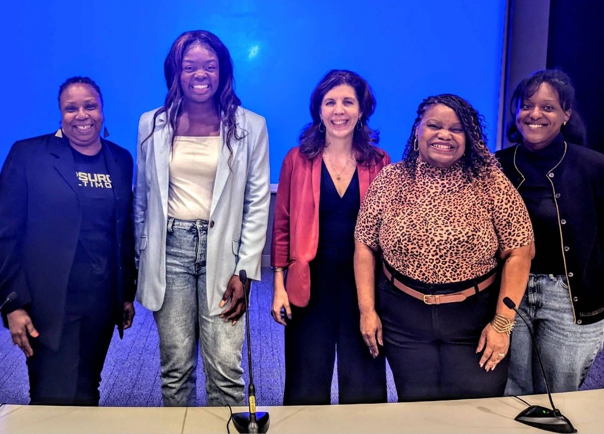 Five smiling women of color on a stage