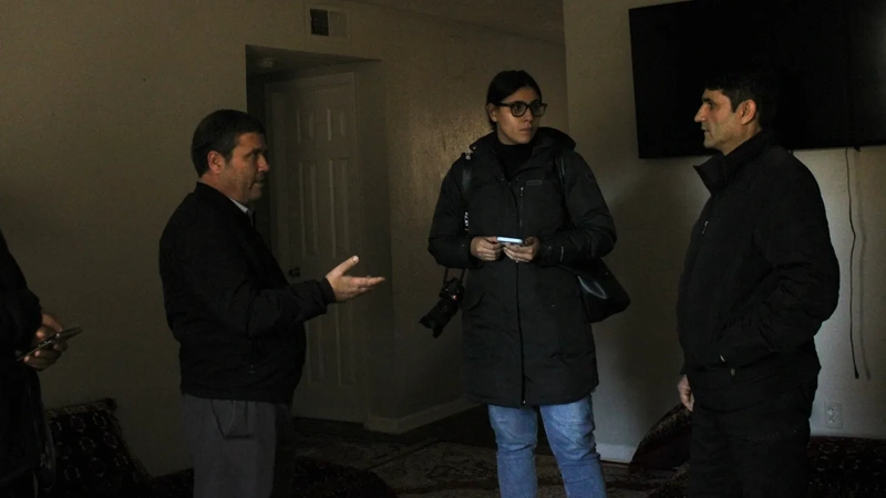 Two men and a woman talking in a darkened room.