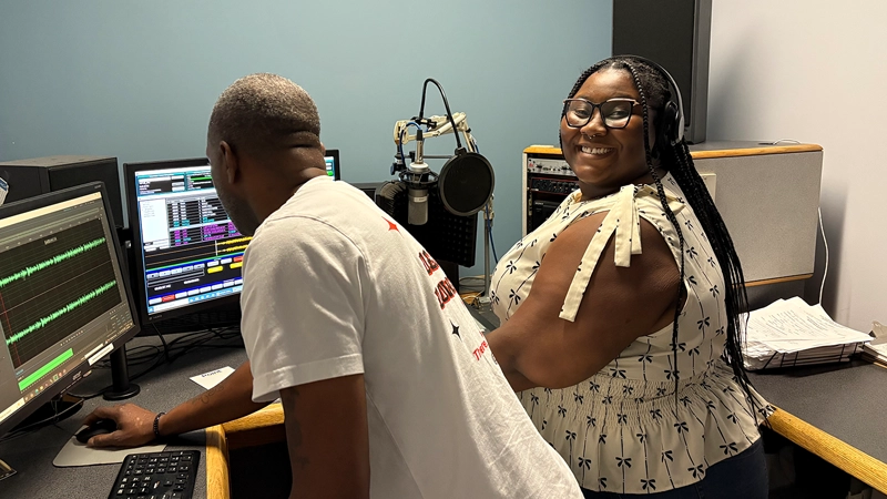 Young Black woman and mature Black man smiling and working in an audio production studio.