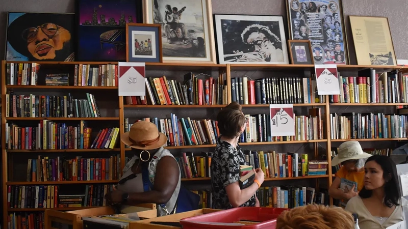 People sitting in a cozy art-vibe bookshop with bookshelves and artwork framed on top of the bookshelves.