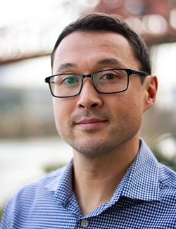 Portrait of man with glasses, short hair and a slight smile.