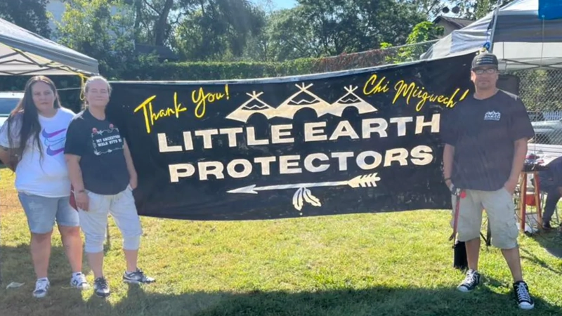 Two women and a man stand smiling in front of a banner that says Thank You! Chi Miigwech! Little Earth Protectors