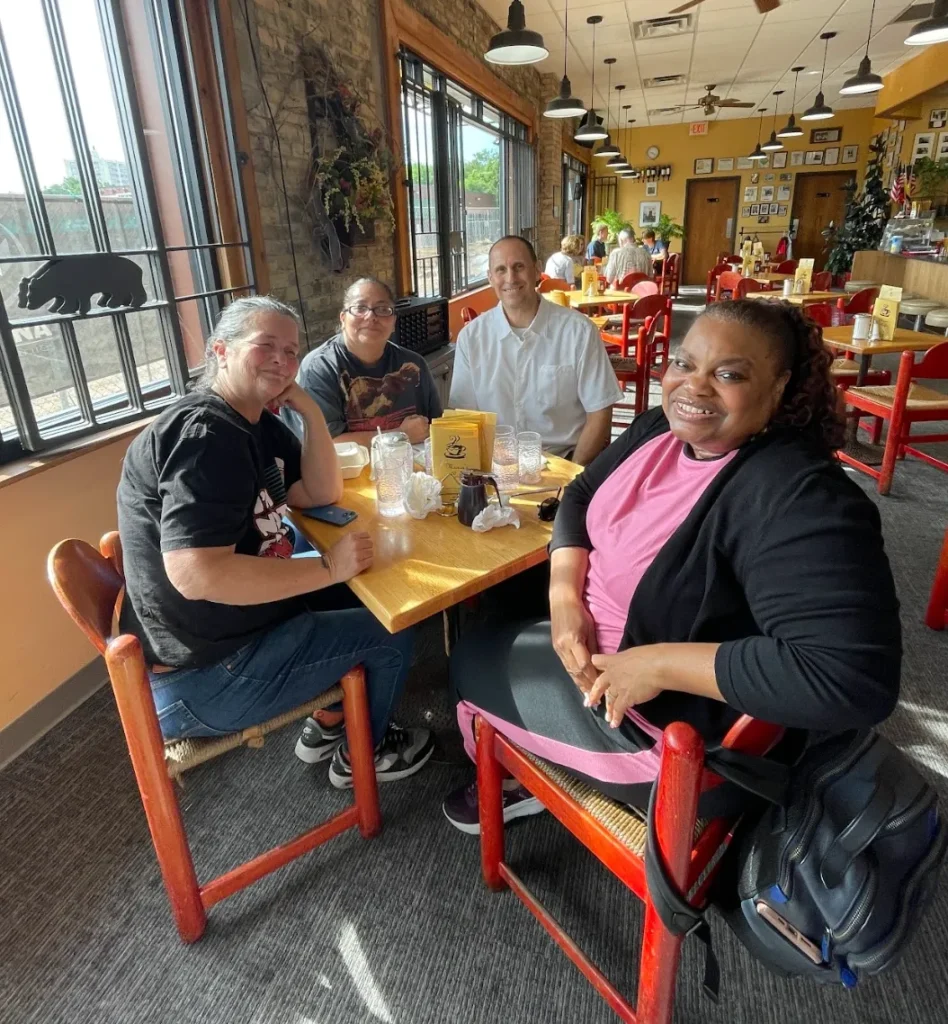 Four people sitting around a table in a restaurant smiling after a meal.