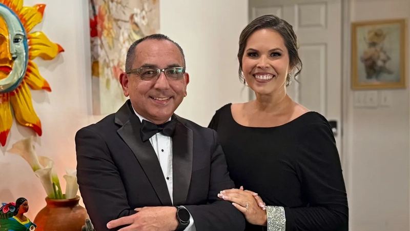 Latina woman in formal dress smiling next to smiling Latino man in a tuxedo.