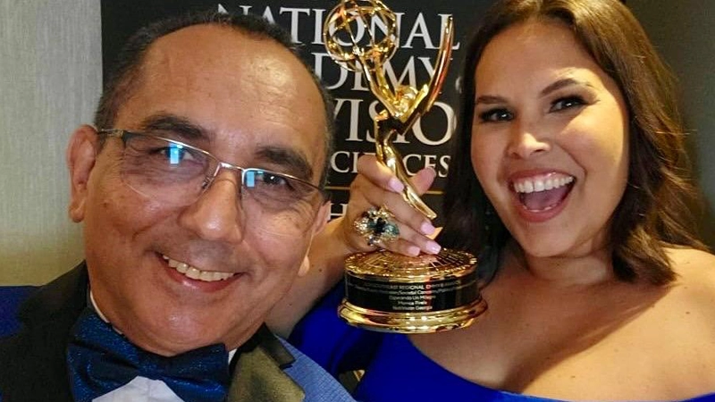 Man and woman in formal black tie wear holding an Emmy award and smiling big.