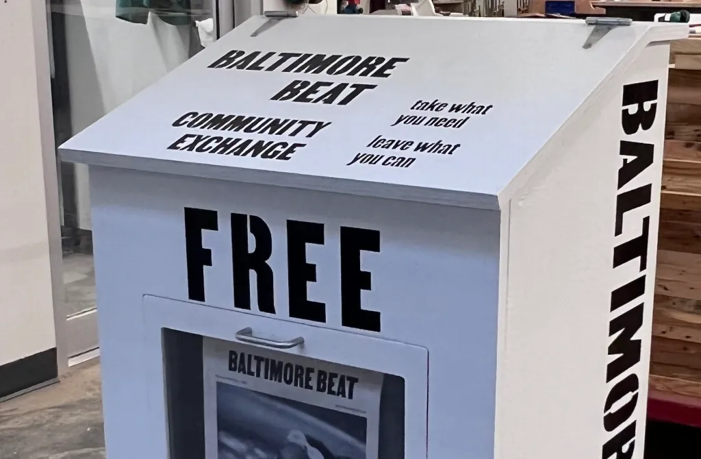 White newspaper box on the street that says Baltimore Beat Free