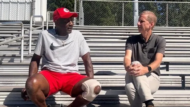 Black man and white man talking sitting on sports field bleacher seats