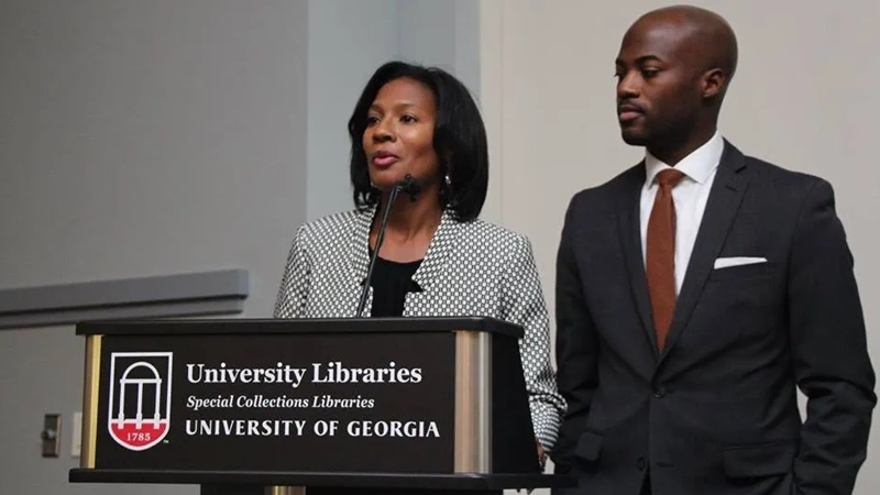 Black woman and Black man dressed in professional suits speak at podium with sign University Libraries, Special Collections, University of Georgia