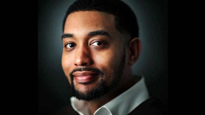 Black man wearing a collared shirt with slight smile