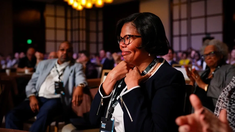 Black woman smiling amidst applause in a presentation room