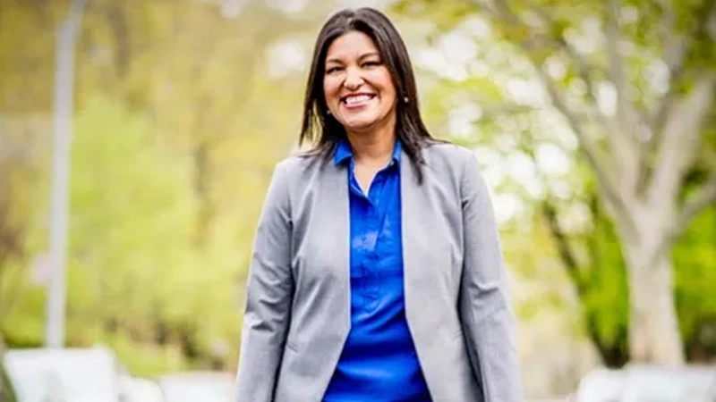 Smiling woman wearing a blazer and blouse walking down the street outdoors.