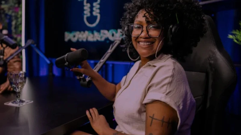 Black woman with natural hair smiling in a podcast studio in front of a microphone.