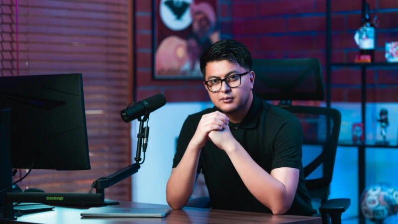 Latino man sitting at a desk with a microphone and a computer